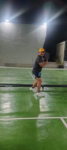 Customer wearing the yellow Ciele GOCap Running Cap while playing a racket sport on a court at night.