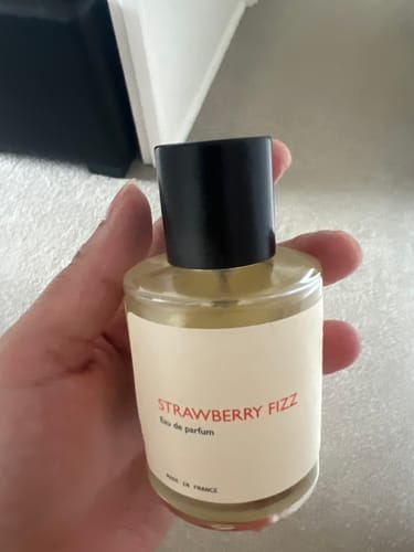 Customer holding the clear glass bottle of Strawberry Fizz eau de parfum indoors.