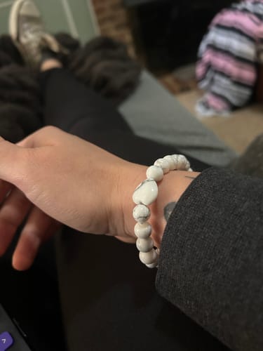 Reviewer's wrist showing the white Howlite bracelet with a heart-shaped bead.