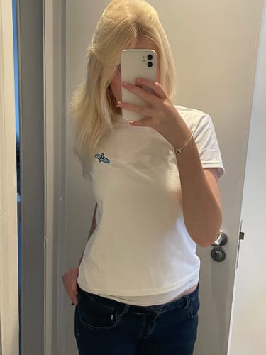 Reviewer in a mirror selfie wearing the white surf's up embroidered baby tee, showing its fit and blue embroidered logo.