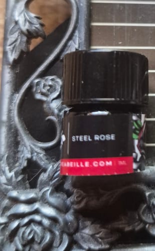 Close-up of the reviewer's small Steel Rose sample bottle resting against a dark, ornate frame.