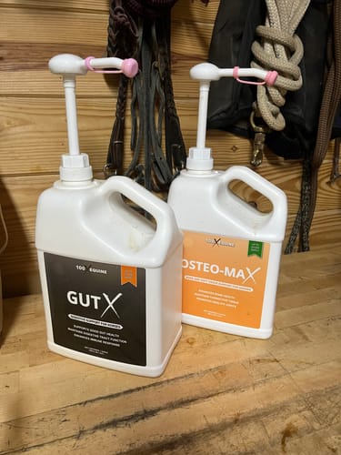 Customer's jug of Gut X supplement with a pump, next to another supplement bottle in a stable.