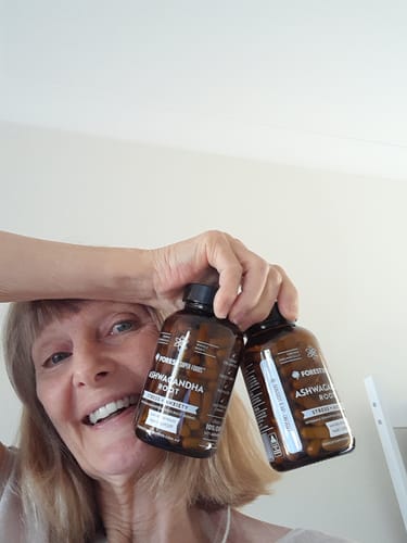 A smiling reviewer holds up two bottles of Organic Ashwagandha Capsules.