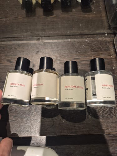 Customer's collection of four perfume bottles from the same brand, lined up on a dark wood surface.