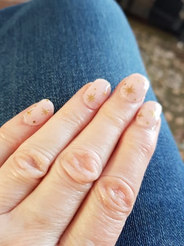 Reviewer's hand showing Golden Stardust nails with a light pink base and gold star decals after one week of wear.