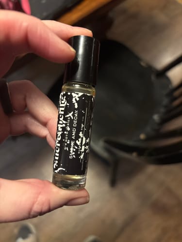 A reviewer holds the small rollerball bottle of Smoke and Decay fragrance in their hand.