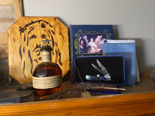 Reviewer's bottle of Blanton's Single Barrel Bourbon displayed on a wooden cabinet among other personal items.