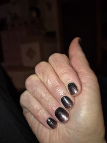 Eine Kundin zeigt ihre fertige Maniküre mit den Pitch Glitter Ombré UV-Gelfolien.