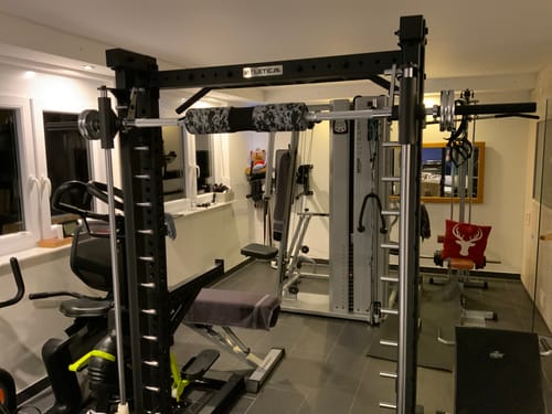 Kunde zeigt das schwarze R7 Saber Squat Rack mit Multipresse, aufgebaut in einem Heim-Fitnessstudio.