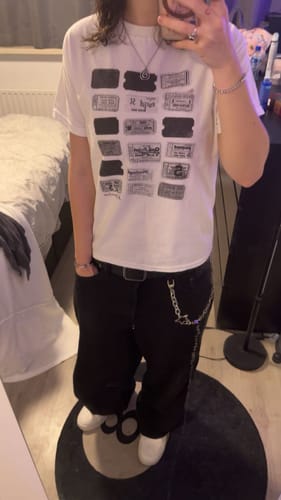Reviewer showing a full-body view of the white one-way ticket baby tee, styled with baggy black pants and a chain.