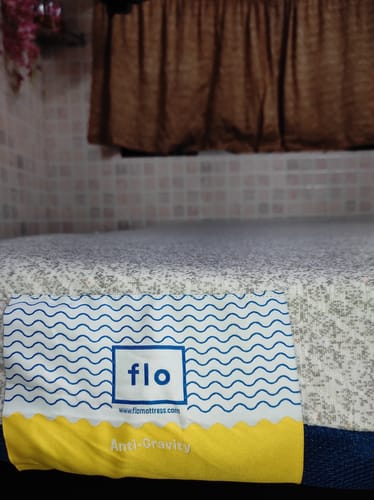 Close-up of the reviewer's Flo Anti-Gravity™ Latex Mattress, focusing on the brand label and patterned white cover.