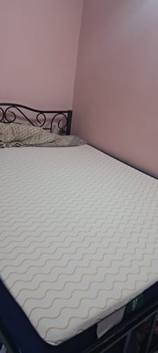 Customer's Flo Mattress Ortho on a bed, showing the white cover with its beige wavy pattern.