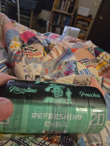 Close-up of a reviewer holding a black and green can of Refreshing Chill Nicotine Pouches.