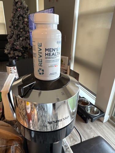 Customer's white bottle of Revive Men's Health supplement resting on a coffee machine in a home setting.