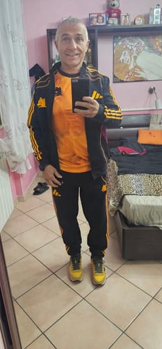 Cliente indossa il completo KIT TUTA ROMA, nero con strisce dorate, in una camera da letto.