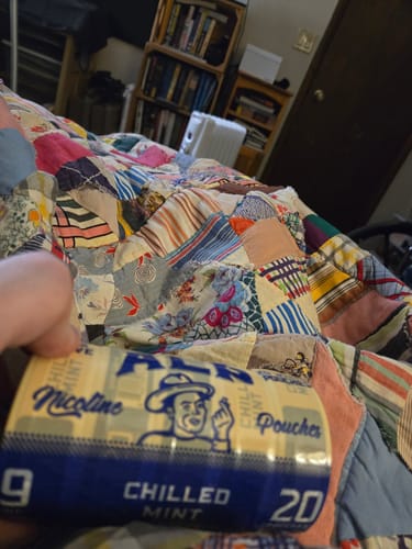 Customer holding a roll of ALP Chilled Mint Nicotine Pouches in front of a colorful patchwork quilt.