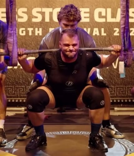 Reviewer performing a heavy squat while wearing black knee sleeves from the Strength Kit.