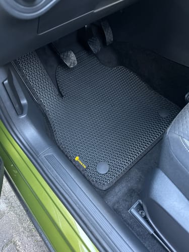 Recenzent pokazuje elegancki, czarny dywanik samochodowy dopasowany do miejsca kierowcy.