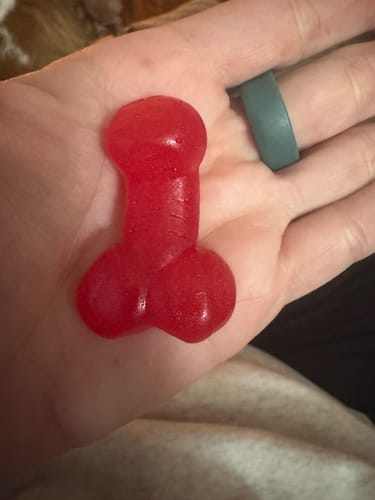 Customer holding a single red penis-shaped gummy from the Bag of Dicks in their hand.