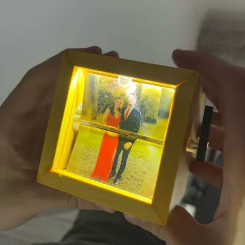 Customer holding the wooden Personalized Photo Box, illuminated by warm light that displays a photo of a couple inside.