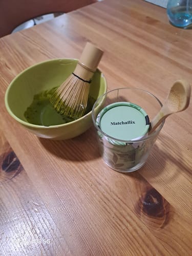 Un cliente preparando su té Matchaflix en un bol verde con un batidor de bambú sobre una mesa de madera.