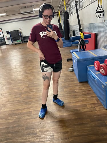 Reviewer at the gym lifting the leg of their 'Divine Strength' shorts to show the inner design.