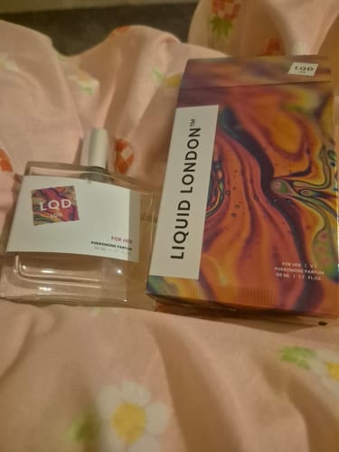 Customer's bottle of For Her Pheromone Perfume next to its colorful box on a floral patterned surface.