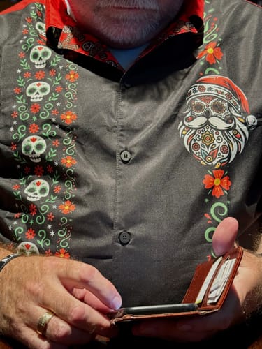 Close-up of a customer wearing the El Sancho Clause Guayabera, showing the sugar skull Santa graphic and floral details.