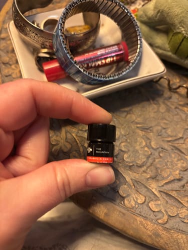 A customer holds up a tiny vial of The Mountain perfume against a background of a carved wooden surface.