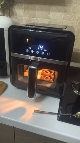Un client arată friteuza sa Air Fryer Novio StonePro neagră în funcțiune, gătind alimente pe blatul de bucătărie.