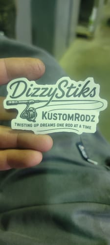Customer's hand holding a custom die-cut sticker with a matte finish, showing a fishing rod and logo for 'DizzyStiks KUSTOMRODZ'.