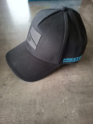 Klant toont de zwarte HD-pet, met het logo op de voorkant en blauwe tekst op de zijkant.