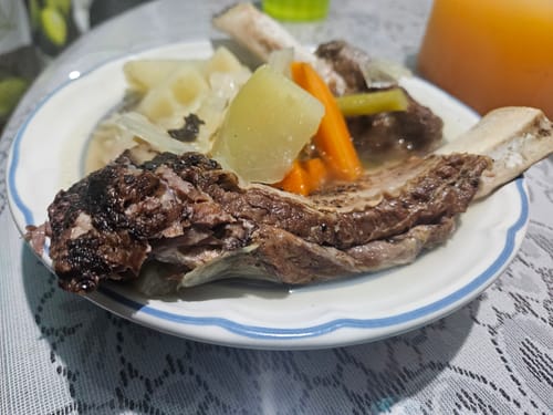 Reseñador muestra sus Costillas Back Ribs servidas en un plato con caldo y verduras.