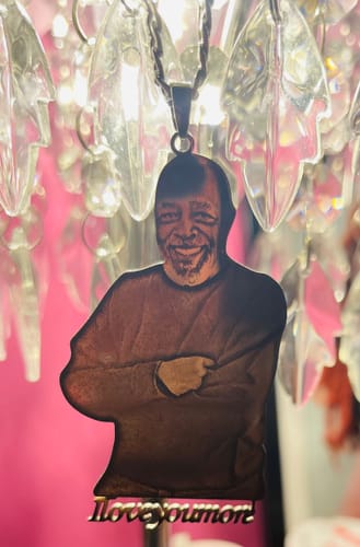 Customer's custom photo engraved pendant necklace with a smiling man's image, hanging from a crystal lamp.