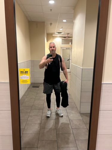 Customer taking a mirror selfie while wearing the black Flex Arm Tank, showing its relaxed fit and long length.