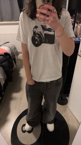 Reviewer in a full-length mirror selfie wearing the say cheese baby tee with dark, baggy jeans.