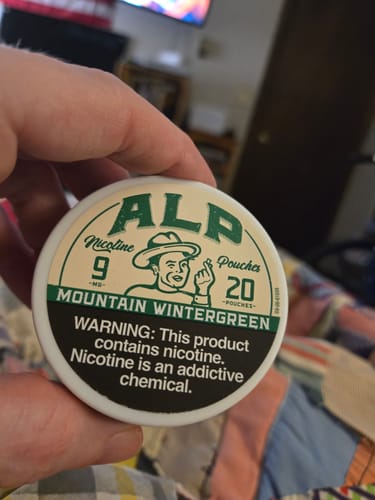 Customer holding a white can of ALP Mountain Wintergreen Nicotine Pouches, showing the green label.