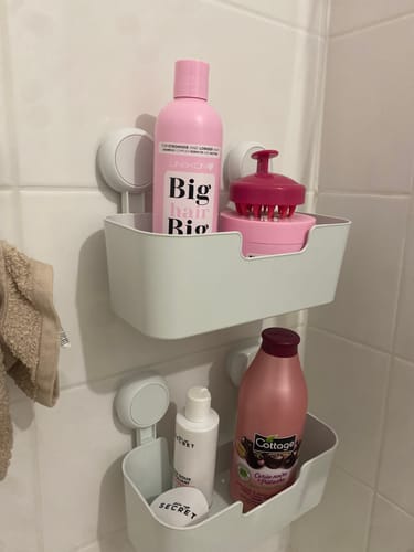 Client montrant le shampooing Gamme The One rose dans un organisateur de douche à côté d'une brosse de massage.