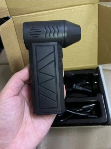 Customer holding the compact black Turbo LED Blower in their hand over its open packaging.