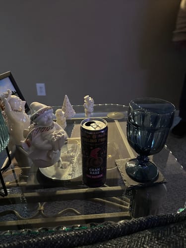 Customer's open can of Cran Razz THC Seltzer on a glass table next to festive holiday figurines.