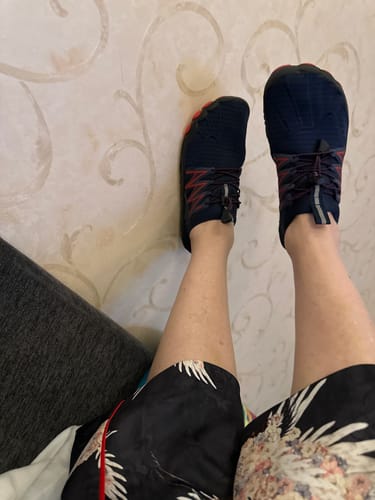 Reviewer's view of their feet wearing a pair of dark blue BareEase shoes with red details.