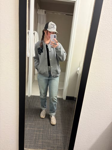 Customer takes a mirror selfie showing the front of the Grey NFR Bomber, styled with jeans and a cap.