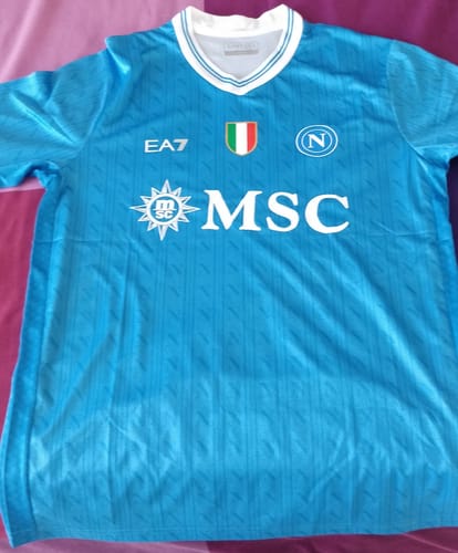 Recensore mostra la Maglia Napoli Home azzurra distesa. In evidenza la patch dello scudetto e lo sponsor MSC sul petto.