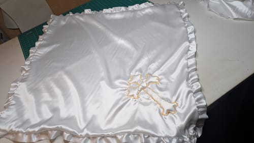 Customer's finished baptism blanket made from white Liquid Satin Fabric, with a ruffled border and gold cross appliqué.