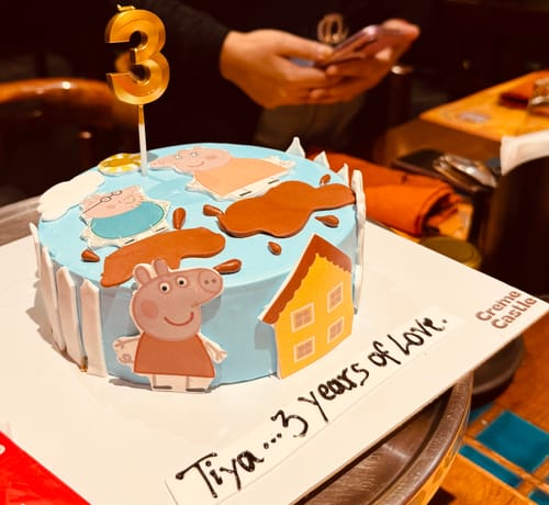 Customer's Peppa pig photo cake with light blue frosting, character cutouts, and a large gold number 3 candle.