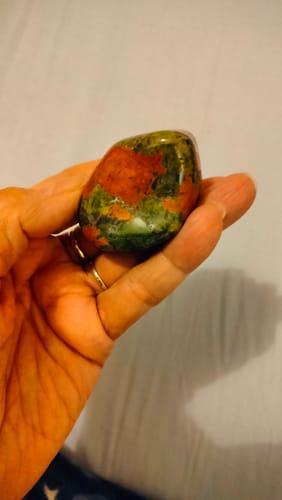 Une cliente tenant une grande pierre Unakite polie, verte et rose, dans le creux de sa main.