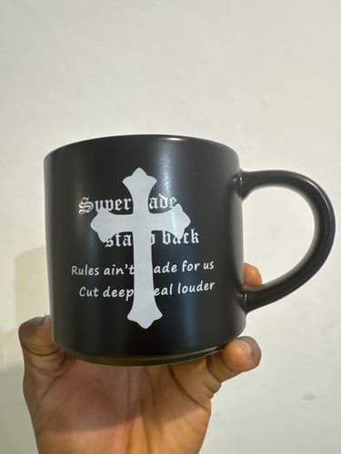 Reviewer holding the black mug, showing its white gothic cross and text.