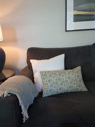 Customer's Gracie in Green floral pillow cover styled on a dark couch with a white pillow.