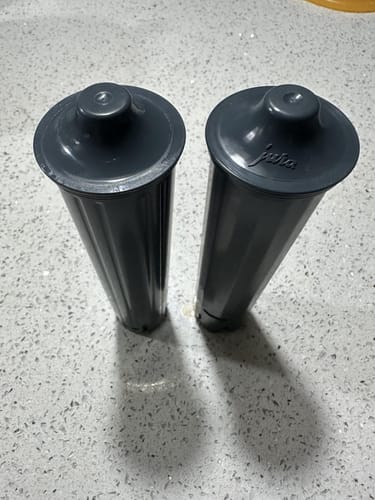 Reviewer's side-by-side comparison of the replacement water filter and the original Jura filter on a countertop.
