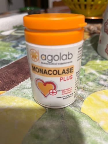 Recensore mostra un flacone bianco di Monacolase PLUS con un tappo arancione brillante su un tavolo.